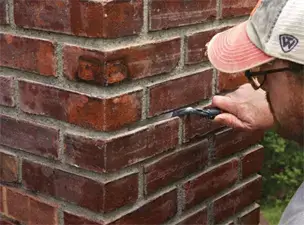Mason brick pointing the mortar joints of a brick wall corner in NYC